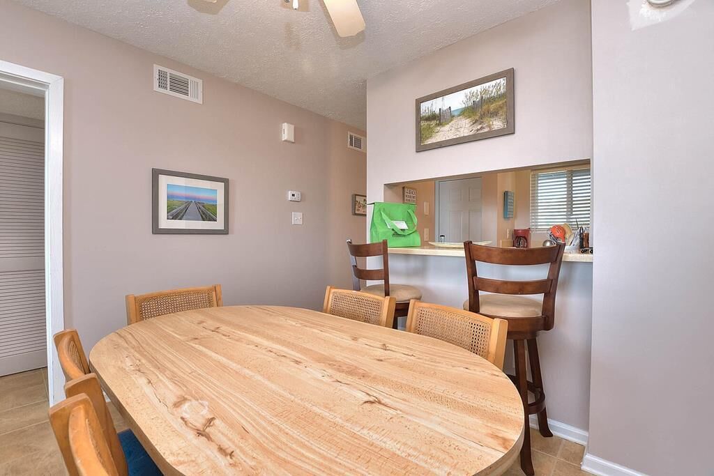 A dining area with a wooden table and chairs, a framed picture on the wall, and a window with blinds.