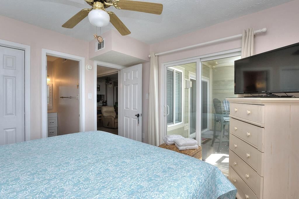 Une chambre à coucher comprenant un lit, une télévision, une commode et un ventilateur de plafond.