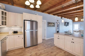 A kitchen with wooden beams, a stainless steel refrigerator, and white cabinetry.