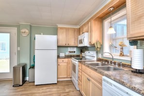 Une cuisine avec des meubles de rangement en bois, un réfrigérateur blanc, un four à micro-ondes, une cuisinière et un évier.
