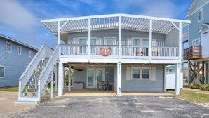 A two-story building with a covered front porch, a staircase to the upper level, and a small table outside. - Charming 2BR duplex with ocean views in Oak Island, perfect for family getaways. (Oak Island)