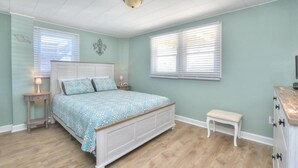 A bedroom with a bed, bedside tables, a bench, and a dresser. - Charming 2BR duplex with ocean views in Oak Island, perfect for family getaways. (Oak Island)