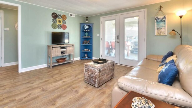 A living room with a sofa, a television, a coffee table, and a decorative wall piece. - Charming 2BR duplex with ocean views in Oak Island, perfect for family getaways. (Oak Island)