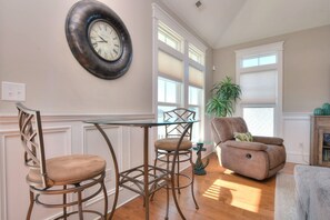 Un comedor con un reloj de pared redondo, una mesa de comedor, dos sillas, un sillón con reposeras y una planta en maceta.