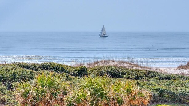 Un velero en aguas oceánicas tranquilas con una playa al frente.