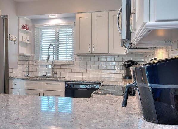 A kitchen with white cabinets, a window with blinds, a dishwasher, and a stainless steel sink.