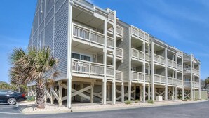 Un edificio de varios pisos con balcones, una palmera y un coche estacionado.