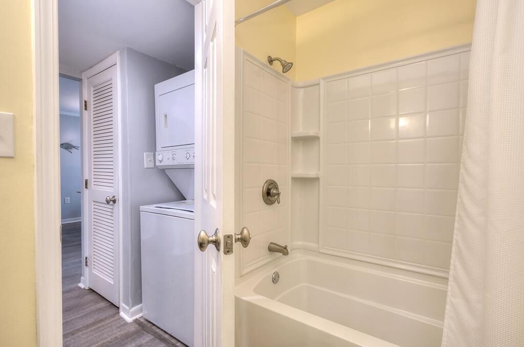 A bathroom with a white bathtub, a shower, and a white door leading to another room.