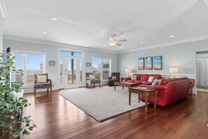 A spacious living room with hardwood floors, a red sofa, a coffee table, and a ceiling fan.