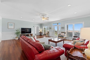 A spacious living room with a red leather sofa, a television, and a ceiling fan.