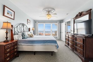 Ein Schlafzimmer mit Bett, Schminktisch, Deckenventilator und großem Fenster.