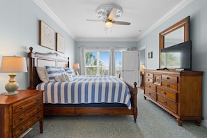 A bedroom with a bed, dresser, TV, ceiling fan, and window.