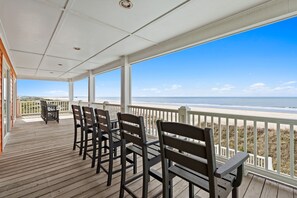 A wooden deck with chairs and a table, overlooking a beach and ocean.