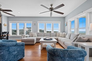 A living room with a sectional sofa, two blue patterned armchairs, a white coffee table, and a ceiling fan.