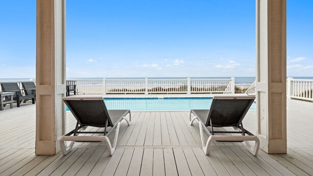 Une terrasse en bois avec deux chaises longues donnant sur une piscine et une plage.