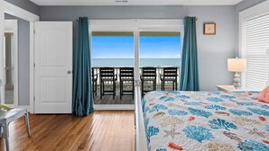 Une chambre avec un lit, une table de chevet, une lampe, une vue sur l’océan par une porte coulissante et une chaise à l’extérieur.