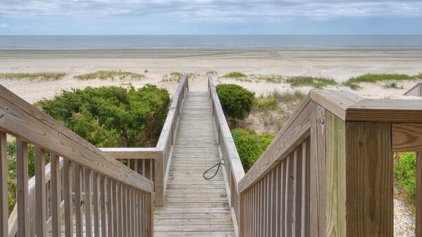 A wooden boardwalk leading to a beach with a view of the ocean.