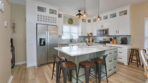A modern kitchen with white cabinets, a central island with stools, stainless steel appliances, and pendant lighting.