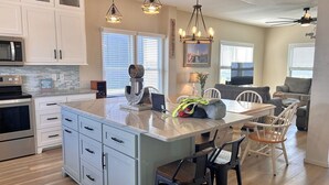 A modern kitchen with white cabinets, a large island, bar stools, and a dining area with a gray sofa.