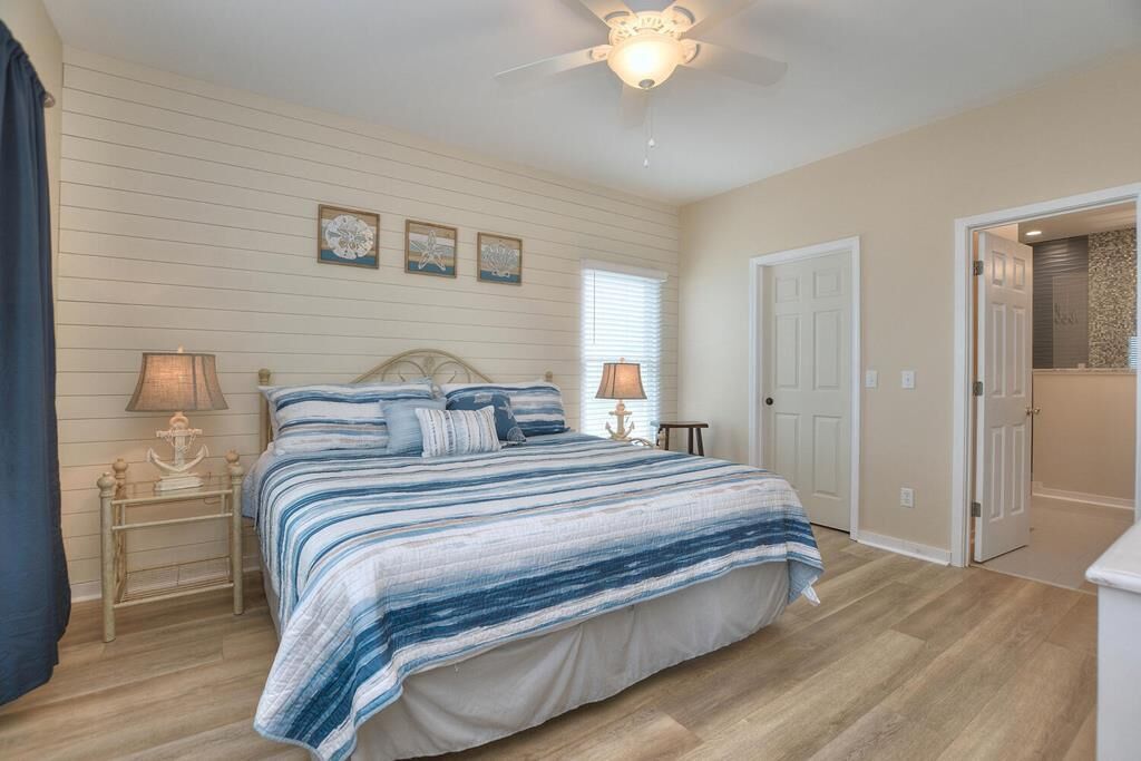 A bedroom with a bed, two bedside tables, a ceiling fan, and a door leading to another room.
