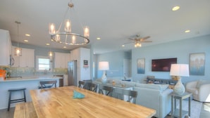 A spacious living area with a wooden dining table, a sofa, and a television. - Oceans Eleven 03: Stunning 5BR oceanfront home in Oak Island, perfect for families! (Oak Island)