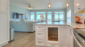 A modern kitchen with white cabinetry, a central island, pendant lighting, and a ceiling fan. - Oceans Eleven 03: Stunning 5BR oceanfront home in Oak Island, perfect for families! (Oak Island)
