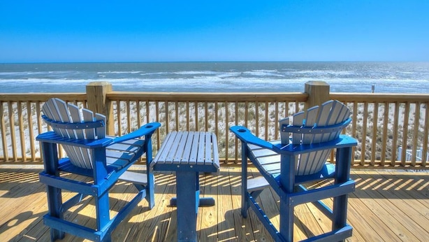 A wooden deck with two Adirondack chairs and a table, overlooking the ocean. - Oceans Eleven 03: Stunning 5BR oceanfront home in Oak Island, perfect for families! (Oak Island)