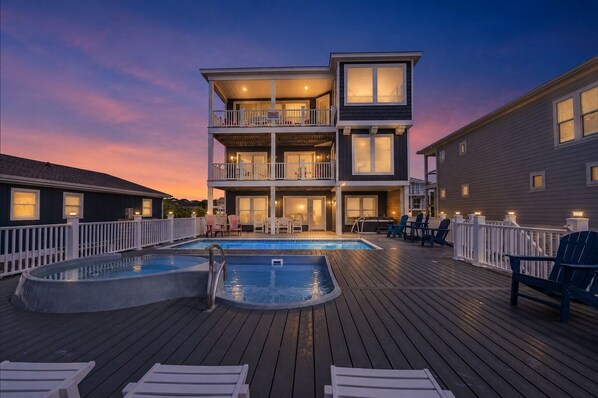 A two-story building with a pool, deck chairs, and a white fence.