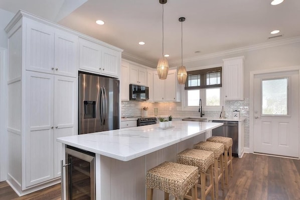 A modern kitchen with white cabinetry, stainless steel appliances, a large island with bar stools, and pendant lighting.