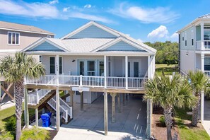 A two-story house with a covered porch and a small deck. - Experience ocean views at "Footprints in the Sand," a cozy 3BR retreat in Oak Island. (Oak Island)