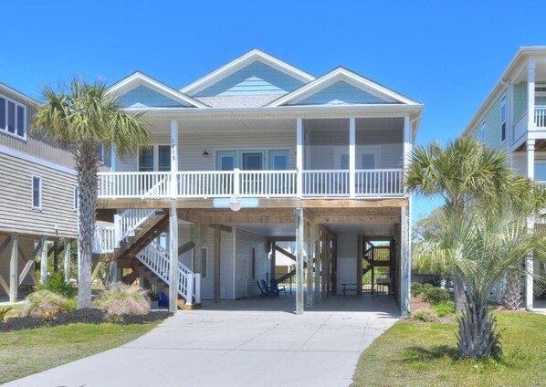 A two-story beachfront building with a covered entrance and a balcony. - Experience ocean views at "Footprints in the Sand," a cozy 3BR retreat in Oak Island. (Oak Island)