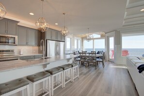 A modern kitchen with a central island, bar stools, and a dining area with a view of the ocean.