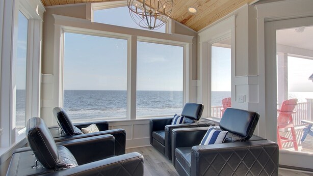 A sunroom with large windows, leather chairs, and a wooden ceiling.