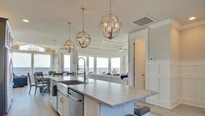 A modern kitchen with a large island, pendant lights, and a view of the ocean.