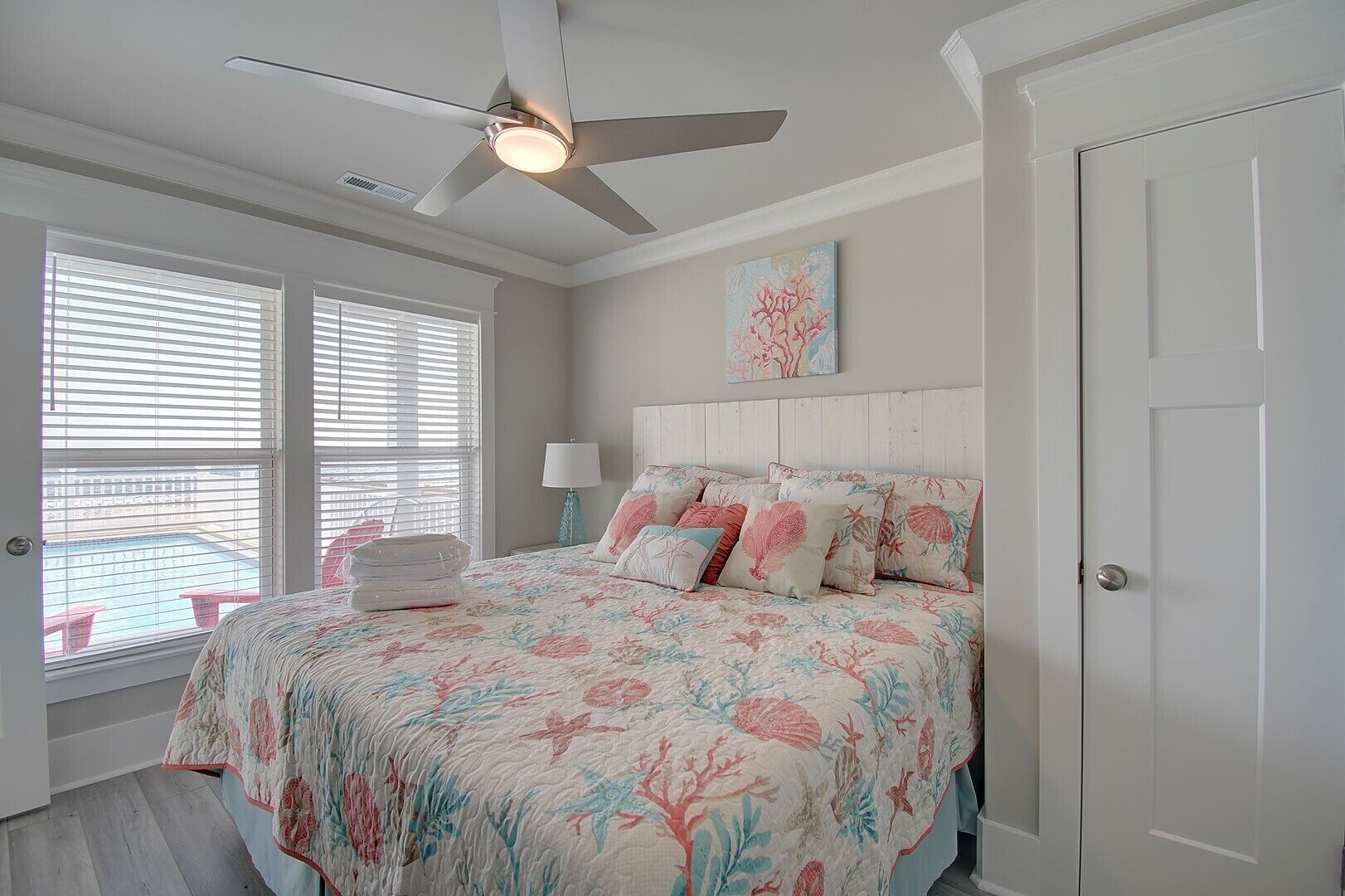 A bedroom with a bed, a ceiling fan, a window with blinds, and a door.