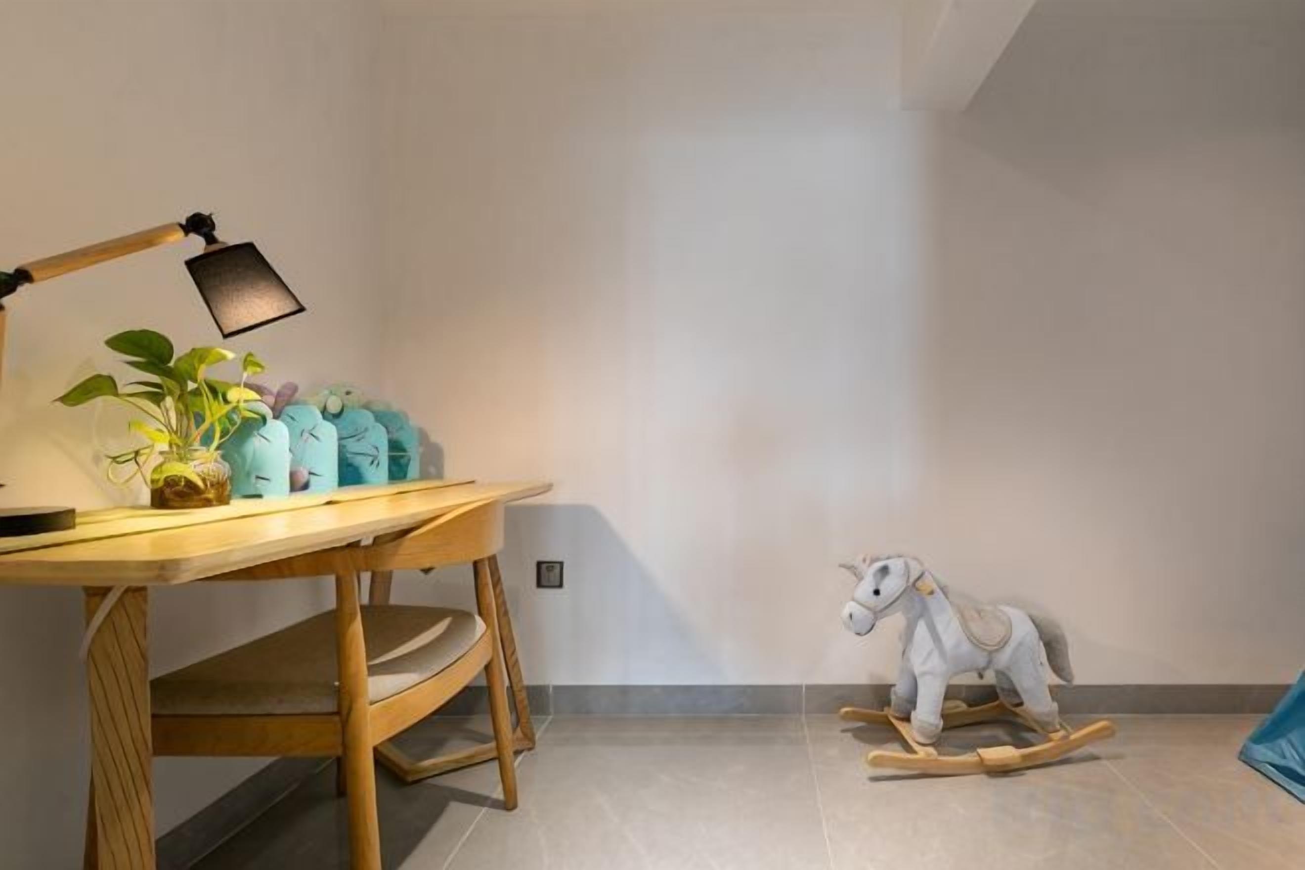 A room with a wooden desk, a desk lamp, a potted plant, and a rocking horse.