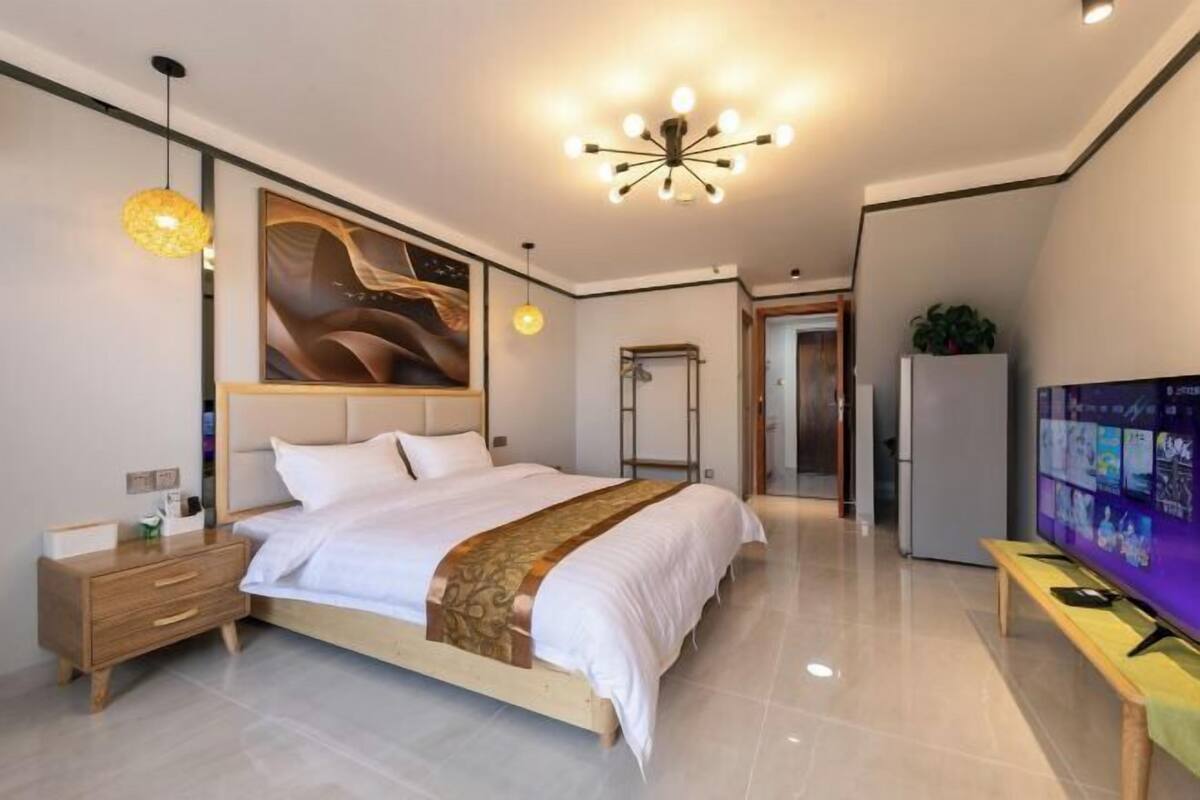A modern bedroom with a large bed, bedside tables, a TV, and a ceiling light fixture.