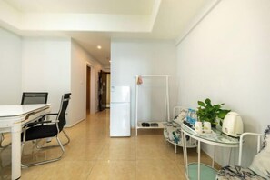 A modern, well-lit room with a dining table, chairs, a refrigerator, a small table with a plant, and a bed. - Gelandi Holiday Apartment (Haikou)