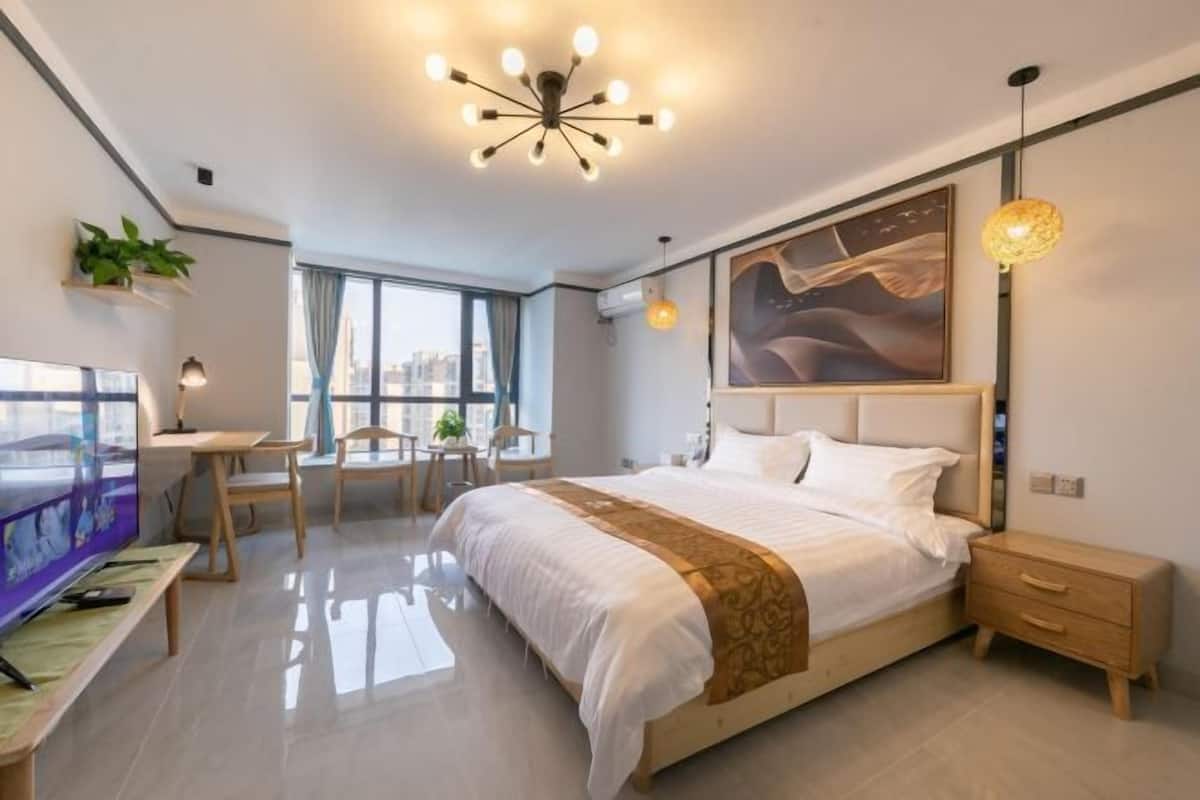 A modern hotel room with a large bed, a desk, a chair, and a TV.