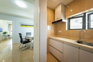 A modern kitchen with a window, a sink, and a dining area with a table and chairs. - Gelandi Holiday Apartment (Haikou)