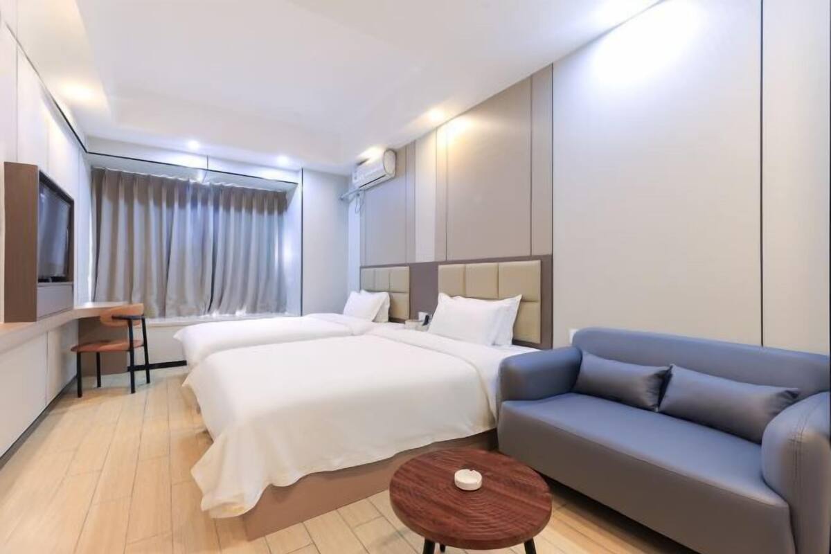 A hotel room with two beds, a sofa, a small table, and a TV.