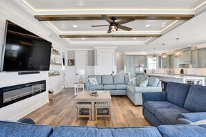 Un salon moderne avec un canapé d’angle, un téléviseur à écran plat, une cheminée et un ventilateur de plafond.