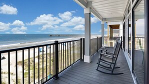 Un balcone con vista sulla spiaggia e l'oceano, dotato di un pavimento in legno e una poltrona a dondolo.