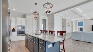 A modern kitchen with a central island, stainless steel appliances, and pendant lighting. - Spacious oceanfront 7-bedroom home on Oak Island, perfect for large gatherings. (Oak Island)