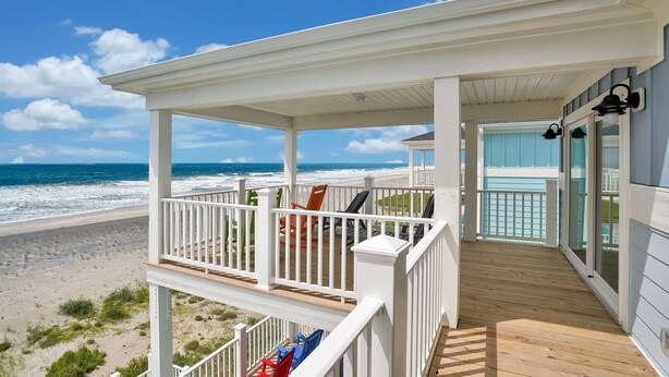 A beachfront property with a covered porch, wooden deck, and ocean view. - Spacious oceanfront 7-bedroom home on Oak Island, perfect for large gatherings. (Oak Island)