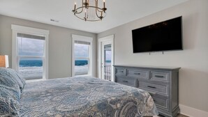 A bedroom with a bed, a dresser, a television, and large windows with a view of the ocean. - Spacious oceanfront 7-bedroom home on Oak Island, perfect for large gatherings. (Oak Island)
