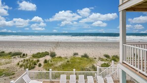A beach view from a balcony with white railings and lounge chairs. - Spacious oceanfront 7-bedroom home on Oak Island, perfect for large gatherings. (Oak Island)