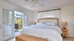 Ein Schlafzimmer mit Bett, Deckenventilator, Nachttisch, Lampe und Blick ins Freie.