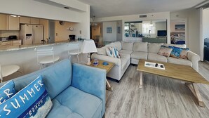 A modern living room with a sofa, a coffee table, and a dining area with a kitchen in the background. - Ocean Harbor by Distinctive Beach Rentals (Fort Myers Beach)