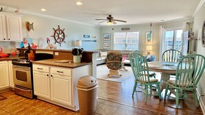 A spacious kitchen with a dining area, a ceiling fan, and a view of the outside. - OW 3201-Flirty Flamingo: Oceanview condo in Oak Island, sleeps 10, pet-friendly. (Oak Island)